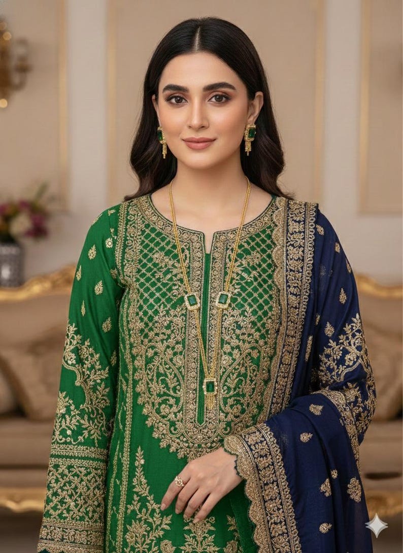May include: A green embroidered dress with gold detailing and a navy blue shawl. The dress features intricate gold patterns on the bodice and sleeves. A gold necklace with square pendants and matching earrings complete the look. The outfit is suitable for special occasions.