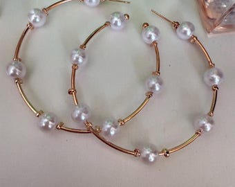 May include: A pair of large gold hoop earrings with white pearl accents. The hoops are thick and have a smooth finish. The pearls are evenly spaced around the hoops.