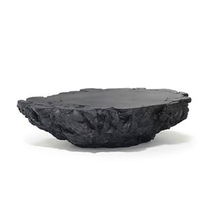 May include: A black coffee table with an irregular, organic shape. The tabletop is smooth, contrasting with the textured, rough edges. The table's dark colour and unique form create a modern, sculptural aesthetic. It is designed to be a statement piece.