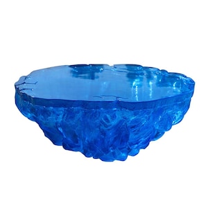 May include: A blue, irregularly shaped glass table with a textured, crystalline appearance. The table has a flat top and a thick, sculpted base, creating a unique, artistic design. The color is a vibrant, transparent blue.