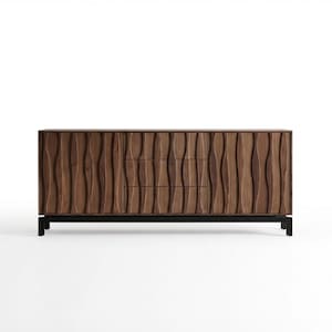Könnte beinhalten: Ein dunkelbrauner Holzschrank mit einem geschnitzten, wellenförmigen Design auf der Vorderseite. Der Schrank hat drei Schubladen und zwei Türen. Er steht auf einem schwarzen Metallsockel und bietet eine moderne Aufbewahrungslösung. Der Schrank ist ca. 183 cm breit.