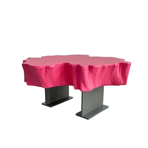 May include: A contemporary coffee table featuring a textured, vibrant pink top. The table is supported by two grey, rectangular metal legs. The table's dimensions are not visible in the image.