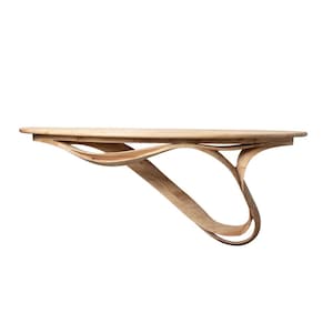 Puede incluir: Una mesa de pared de madera clara con un diseño curvo y fluido. La mesa tiene una parte superior redondeada y una base escultural única. La veta de la madera es visible y la mesa parece estar hecha de una sola pieza de madera.
