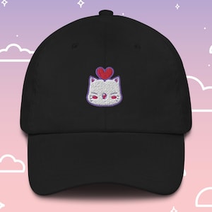 Puede incluir: Una gorra de béisbol negra con un gato blanco bordado con un corazón rojo en la cabeza. El gato tiene ojos morados y una nariz rosa.
