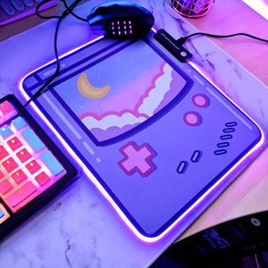 Könnte beinhalten: Eine violette und rosafarbene Gaming-Mausmatte mit einem Retro-Spielekonsolendesign. Die Mausmatte hat einen hellblauen Rand und einen leuchtend violetten Rand. Der Text "LED Digital Controller Pad" ist auf der Mausmatte sichtbar.