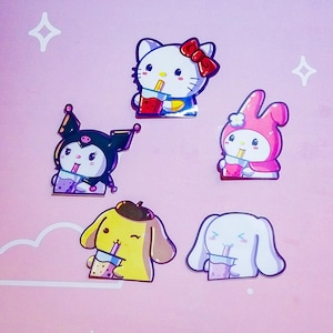 Peut inclure: Cinq autocollants de personnages de dessins animés colorés sur fond rose. Les autocollants présentent des personnages avec des boissons, dont un chat avec un nœud rouge, un personnage noir, un lapin rose, un chien jaune et un lapin blanc.