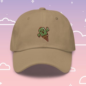 Könnte beinhalten: Eine beige Baseballkappe mit einem gestickten grünen Kaktus, der einen Eisbecher auf dem Kopf trägt.