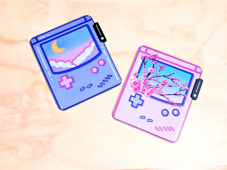 May include: Two gameboy-style phone cases, one with a pink background and a cherry blossom design, and the other with a blue background and a night sky design.