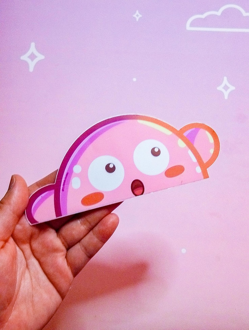 Puede incluir: Un personaje rosa de estilo caricatura con grandes ojos blancos, una expresi&oacute;n de sorpresa y peque&ntilde;as mejillas naranjas. El personaje tiene una forma curva con protuberancias en forma de oreja a cada lado. El fondo es rosa claro con estrellas blancas y una nube.