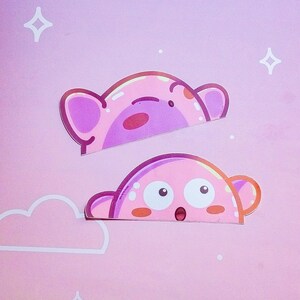 Puede incluir: Dos pegatinas rosas con personajes de dibujos animados con forma de oso. La pegatina superior tiene una expresi&oacute;n de ojos cerrados, mientras que la pegatina inferior tiene ojos grandes y la boca abierta. El fondo es un degradado rosa con formas de nubes y estrellas blancas.