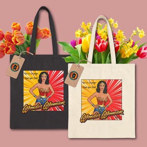 May include: Two tote bags, one black and one off-white, each featuring a Wonder Woman graphic. The graphic includes the text "You're stronger than you think" and "Wonder Woman." Both bags have handles and are filled with colorful flowers.