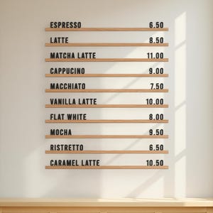 以下が含まれることがあります： 白い壁に表示されたコーヒーショップのメニュー。エスプレッソ、ラテ、モカなど、さまざまなコーヒーの飲み物が価格とともに表示されています。メニューは黒い文字の木製のスラットでできています。画像の下部には木製のキャビネットが表示されています。
