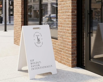 May include: A white A-frame sidewalk sign featuring a black circular logo with the text Leaf Petal Stem The Tea Garden and the letters LPS. Below the logo, the text reads Sip Boldly. Savor Intentionally. The sign has a handle cutout at the top.