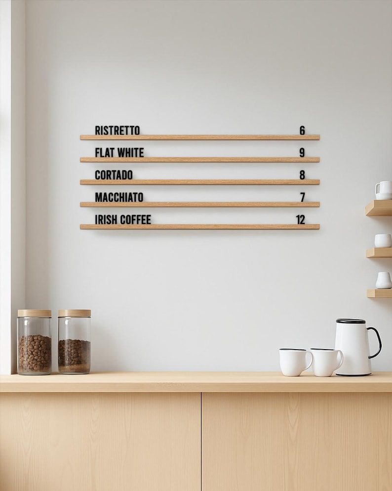 May include: A wall-mounted wooden menu board featuring five horizontal shelves with black lettering. The text reads RISTRETTO 6, FLAT WHITE 9, CORTADO 8, MACCHIATO 7, and IRISH COFFEE 12. The board is made of light-toned wood with a natural grain finish.
