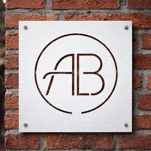 K&ouml;nnte beinhalten: Ein quadratisches wei&szlig;es Schild mit den Buchstaben "AB" in einem Kreis, das an einer Ziegelmauer befestigt ist. Die Buchstaben und der Kreis sind dunkelbraun, und das Schild wird mit vier kleinen silbernen Schrauben befestigt. Die Ziegelmauer ist rotbraun.