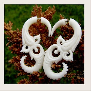 May include: A pair of white bone earrings with intricate carved designs. The earrings are shaped like a curved horn with a decorative pattern.