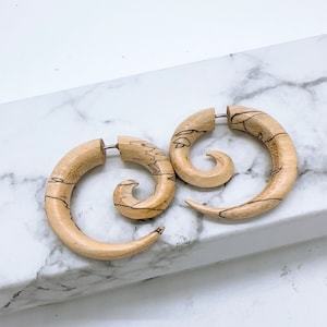 May include: A pair of wooden spiral earrings with a natural wood grain finish. The earrings are a light brown colour and have a unique spiral design.
