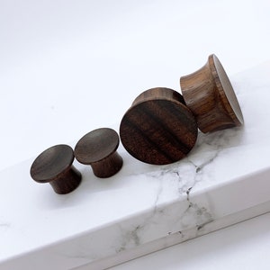 May include: Set of four wooden ear gauges in various sizes. The gauges are made of dark brown wood with a natural grain pattern.