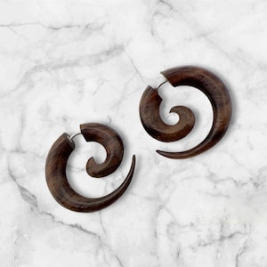 May include: A pair of dark brown wooden spiral earrings. The earrings have a curved, swirling design with a silver-colored post. The wood grain is visible, adding texture to the earrings. These earrings are a unique accessory.