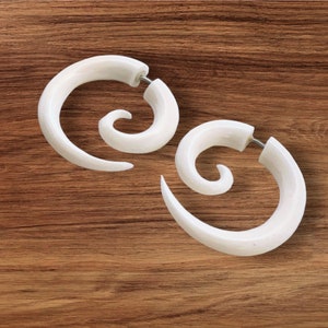 May include: Two white spiral ear gauges, made of a smooth, polished material. The gauges are in the shape of a spiral, with a slightly curved shape.