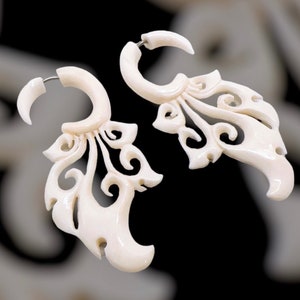 May include: A pair of white bone earrings with intricate carved designs. The earrings are shaped like a leaf with a circular hoop at the top.
