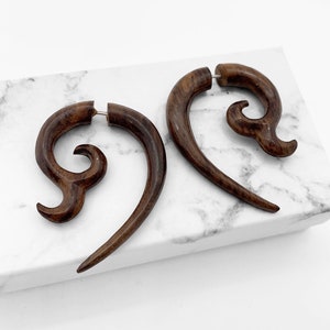 Op de afbeelding: Een paar bruine houten oorbellen met een uniek swirl-ontwerp. De oorbellen zijn gemaakt van natuurlijk hout en hebben een rustieke uitstraling.