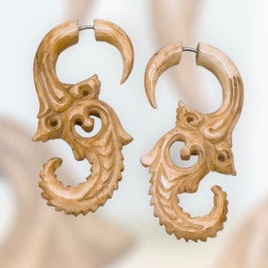 Op de afbeelding: Een paar gegraveerde oorbellen van been met een gedetailleerd, ingewikkeld ontwerp. De oorbellen zijn lichtbeige van kleur en hebben een ronde vorm met een gebogen, decoratieve uitbreiding.