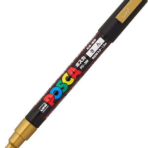 Puede incluir: Un marcador de pintura Posca dorado con un barril negro y una punta blanca. El marcador tiene texto japonés que dice "Posca" y "PC-3M" y "kin", que significa oro en japonés. El marcador tiene un ancho de línea de 0,9 a 1,3 mm.