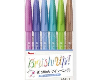 May include: A set of six Pentel Brush Up! Touch Sign Pens in a variety of pastel colors. The pens are packaged in a clear plastic sleeve with the brand name and product name printed on the front.
