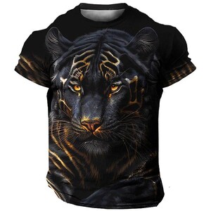 Könnte beinhalten: Schwarzes T-Shirt mit einem detaillierten Bild des Gesichts eines schwarzen Panthers. Der Panther hat goldene Augen und Akzente, die einen Kontrast zum dunklen Hintergrund bilden. Das Shirt hat einen Rundhalsausschnitt.