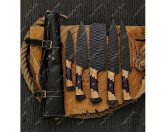 May include: A set of five black kitchen knives with wooden handles and a black leather roll for storage. The knives have a honeycomb pattern on the blades.