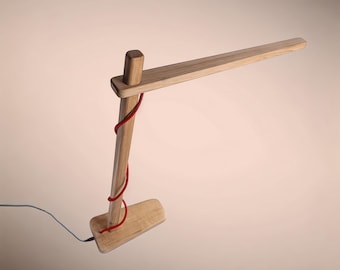 May include: A wooden desk lamp with a red cord wrapped around the base and arm. The lamp has a simple, modern design.