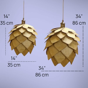 K&ouml;nnte beinhalten: Zwei Holz-Pendelleuchten, eine 35 cm und die andere 86 cm hoch. Jede Leuchte hat ein geschichtetes, bl&uuml;tenblattartiges Design in nat&uuml;rlichen Holzt&ouml;nen, das an einer goldfarbenen Halterung aufgeh&auml;ngt ist. Die Leuchten sind 35 cm und 86 cm breit.