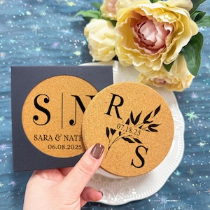 May include: Two round cork coasters with personalized engravings. One coaster features the initials "S" and "N" with the text "Sara & Nath 06.08.2025". The other coaster features the initials "R" and "S" with a leafy branch design and the date "07.18.25".