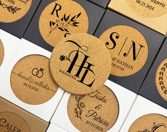 May include: A collection of cork coasters with personalized wedding details. Each coaster features a unique design with initials, names, and wedding dates. The coasters are displayed in their individual boxes.