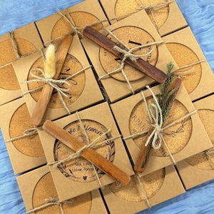 Puede incluir: Un juego de 12 posavasos de corcho personalizados con agitadores de madera, empaquetados en cajas marrones. Los posavasos presentan varios diseños con nombres, fechas y ubicaciones. Los posavasos están atados con cuerda y decorados con ramitas de vegetación.