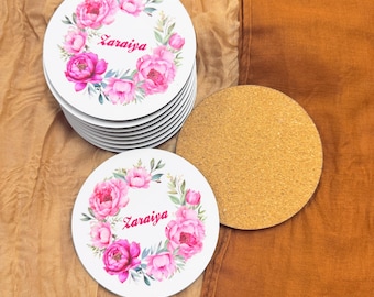 May include: A stack of round white coasters with a floral design and the name "Zarailya" printed in pink. The coasters are surrounded by a cork coaster.