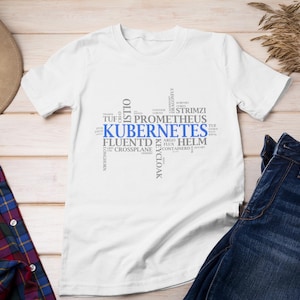 Op de afbeelding: Wit T-shirt met een blauwe en grijze woordwolk die "Kubernetes" zegt. De woordwolk bevat andere gerelateerde termen zoals "Helm", "Fluentd", "Prometheus" en "Keycloak".