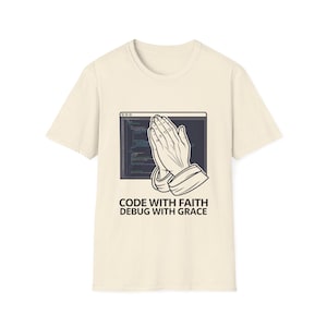 May include: Cream-colored t-shirt featuring a graphic of praying hands in front of a computer screen with code. The text "CODE WITH FAITH DEBUG WITH GRACE" is printed below the graphic. The shirt is made of a soft material.
