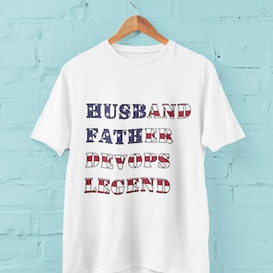 May include: White t-shirt with the text "Husband Father Devops Legend" in red, white, and blue letters, resembling the American flag.