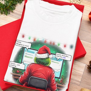 May include: White t-shirt with a cartoon Grinch in a Santa hat, looking at a computer screen. The shirt includes speech bubbles with text: "Santa: Naughty or nice?" and "Grinch: ...just phishing."