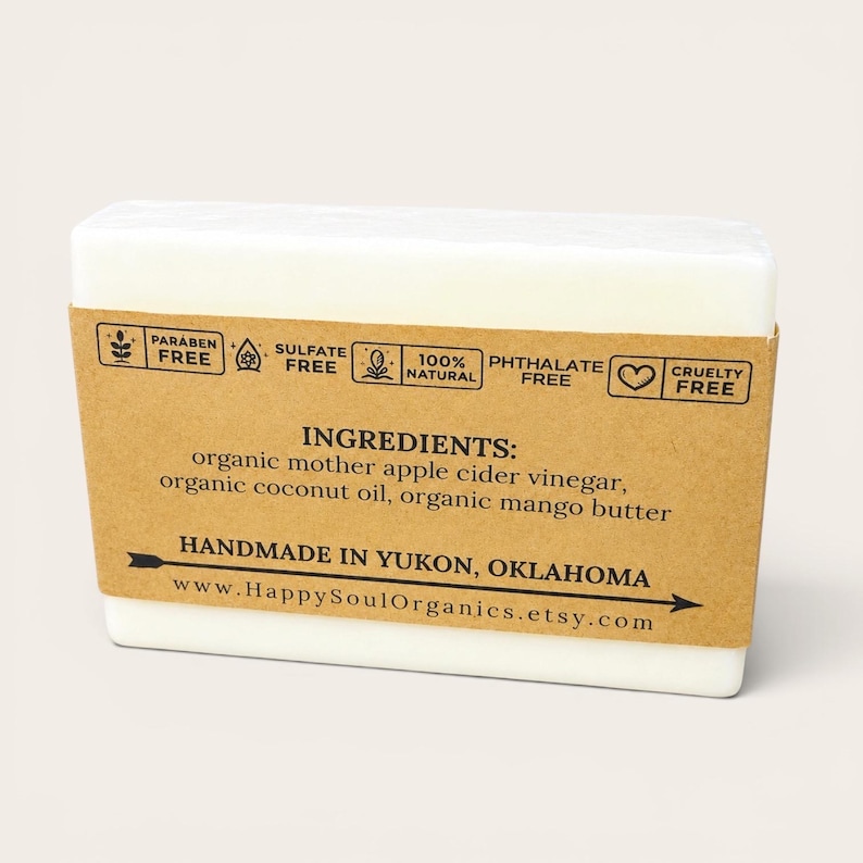 May include: A white rectangular bar of soap with a brown paper label wrapped around it. The label includes text that reads "Paraben Free", "Sulfate Free", "100% Natural", "Phthalate Free", and "Cruelty Free". The ingredients are listed as organic mother apple cider vinegar, organic coconut oil, and organic mango butter.