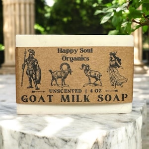 Può includere: Una saponetta di latte di capra bianca con un'etichetta marrone che recita "Happy Soul Organics" e "Unscented | 4 oz Goat Milk Soap". L'etichetta presenta illustrazioni di una capra, una donna con una corona e un uomo con un elmo e una lancia.