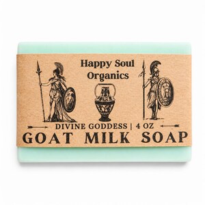 May include: A rectangular bar of light green goat milk soap wrapped in a tan paper label. The label features the text Happy Soul Organics, Divine Goddess, and 4 oz Goat Milk Soap, along with black illustrations of two warriors and a central urn.