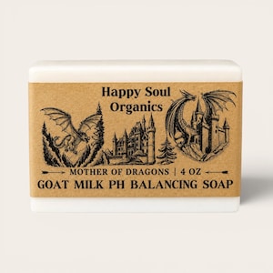 Op de afbeelding: Een rechthoekige zeep van geitenmelk met een bruin etiket met illustraties van draken en een kasteel. Het etiket luidt "Happy Soul Organics" en "Mother of Dragons | 113g GOAT MILK PH BALANCING SOAP."