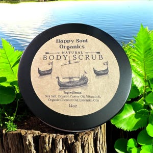 K&ouml;nnte beinhalten: Ein runder schwarzer Beh&auml;lter mit Happy Soul Organics Natural Body Scrub und einem beigen Etikett, das drei Segelschiffe zeigt. Das Etikett listet Inhaltsstoffe wie Meersalz, Bio-Rizinus&ouml;l, Vitamin E, Bio-Kokos&ouml;l und &auml;therische &Ouml;le auf, mit einem Nettogewicht von 397g.