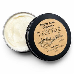 以下が含まれることがあります： Happy Soul Organicsのタローフェイスバームが入った、開いた丸い銀色の缶。バームはクリーム色でオフホワイトです。缶を部分的に覆う黒い蓋には、テキストと農場のイラストが描かれた茶色のラベルが付いています。ラベルには「100% Grass-Fed Beef Tallow」と「2 OZ」と記載されています。
