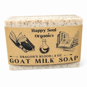 May include: A rectangular bar of off-white goat milk soap with brown speckles, wrapped in a tan paper label. The label features the text Happy Soul Organics, Dragon's Blood, and 4 oz Goat Milk Soap, alongside illustrations of books and a potion bottle.