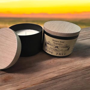 Puede incluir: Dos velas de soja cil&iacute;ndricas negras con tapas de madera clara. Una vela est&aacute; abierta, mostrando cera blanca y una mecha. La otra est&aacute; cerrada con una etiqueta que dice Happy Soul Organics, Pure Soy Candle, 4 oz, Pine Tree y un gr&aacute;fico de paisaje.
