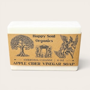 May include: A rectangular bar of white soap with a brown paper label. The label features illustrations of a tree, a building, and figures, along with the text "Happy Soul Organics" and "Apple Cider Vinegar Soap", 4 oz.